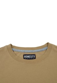 Tan bomulds t-shirt med rund halsudskæring og en grå krave indvendigt. Har et "HONESTY" label i sort på den indvendige halsområde.