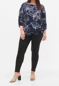 Blouse bleu marine avec un motif floral blanc et un décolleté en trou de serrure, associée à un jean skinny noir et des mules à talons bloc ouvertes beige.