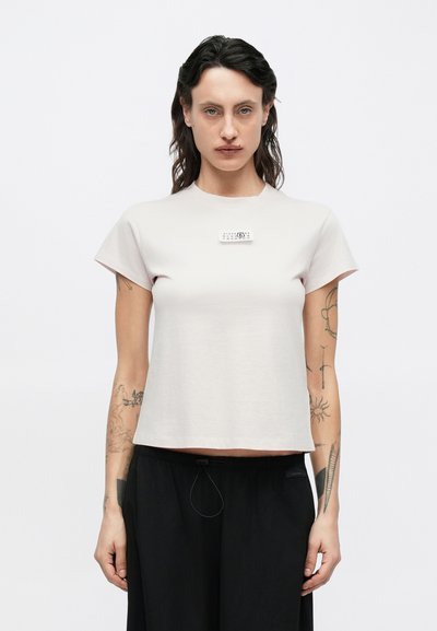 Light pink short-sleeve t-shirt with a round neck and a rectangular label on the chest. Fabric appears smooth and soft in texture.