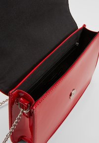 Rød håndtaske i laklæder med magnetlås, indvendig lynlåslomme og sølvkæderem. Glat tekstur med rene linjer.