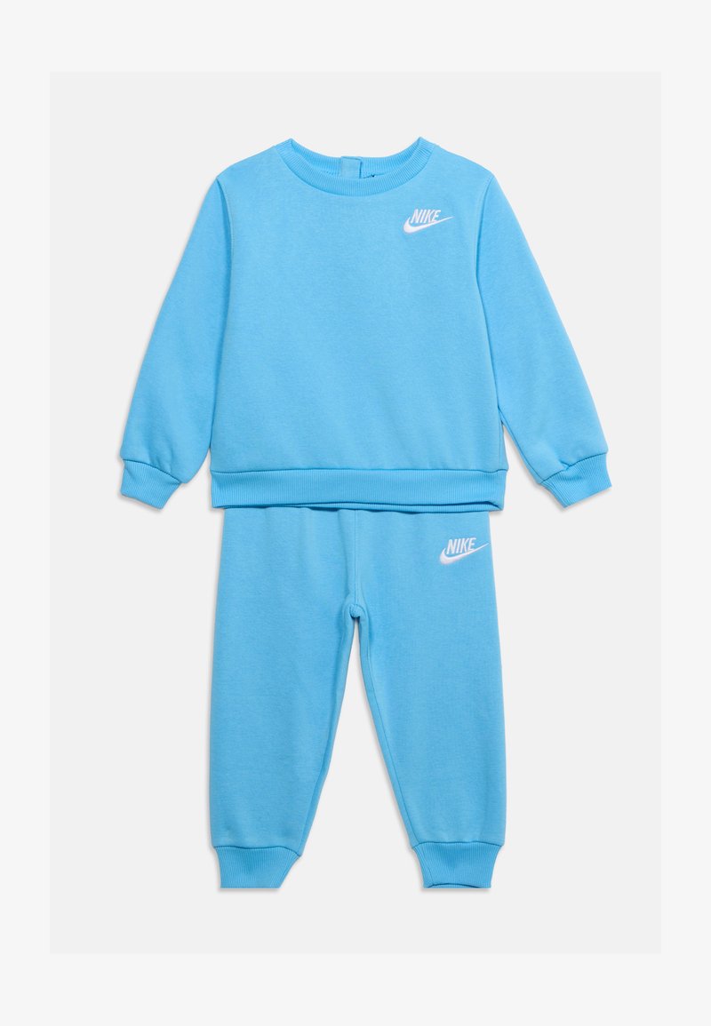 Σετ παιδικό φούτερ και παντελόνι φόρμας Nike σε ανοιχτό μπλε χρώμα με λευκά λογότυπα Nike στο στήθος και στο μηρό, με ριμπ μανσέτες και στρογγυλή λαιμόκοψη.