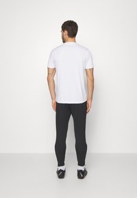 Weißes Kurzarm-T-Shirt, kombiniert mit schwarzen Slim-Fit-Hosen, getragen mit schwarzen Sportschuhen und weißen Knöchelsocken, von hinten gezeigt.
