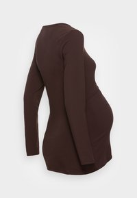 Maglia premaman a maniche lunghe di color marrone scuro. Realizzata in tessuto morbido ed elastico, presenta un colletto rotondo e una silhouette aderente e curvata.