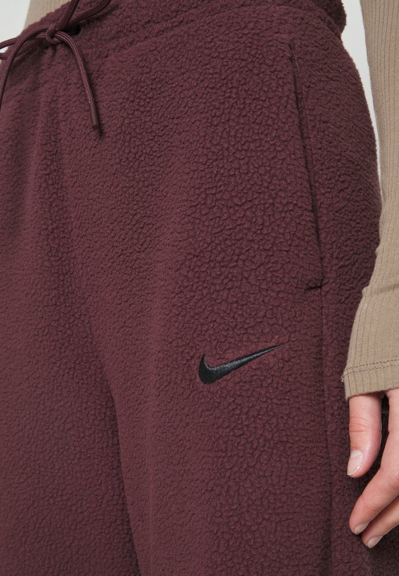 Pantalons de jogging en polaire bordeaux avec une surface texturée, présentant un logo Nike noir et une ceinture à cordon pour un ajustement réglable.