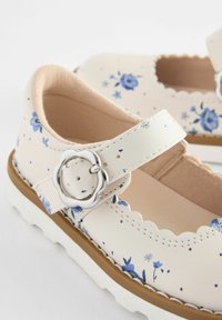 Weiße Mary Jane-Schuhe mit Blumenmuster und blauen Blumen, gewellten Kanten, einer silbernen Schnalle und einer strukturierten Gummisohle.
