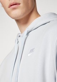 Ljusblå hoodie i mjukt tyg med dragsko-huva och en liten, broderad vit Nike-logga på br östet.