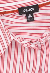 Korte mouwen shirt met rode en witte strepen, gemaakt van lichtgewicht stof. Bevat een label met het "J&JOY"-logo en maatdetails.