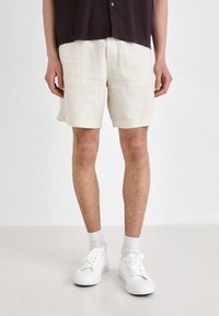 Szorty lniane w kolorze off-white, z luźnym krojem i długością do kolan, połączone z białymi sneakersami i skarpetkami do kostek.