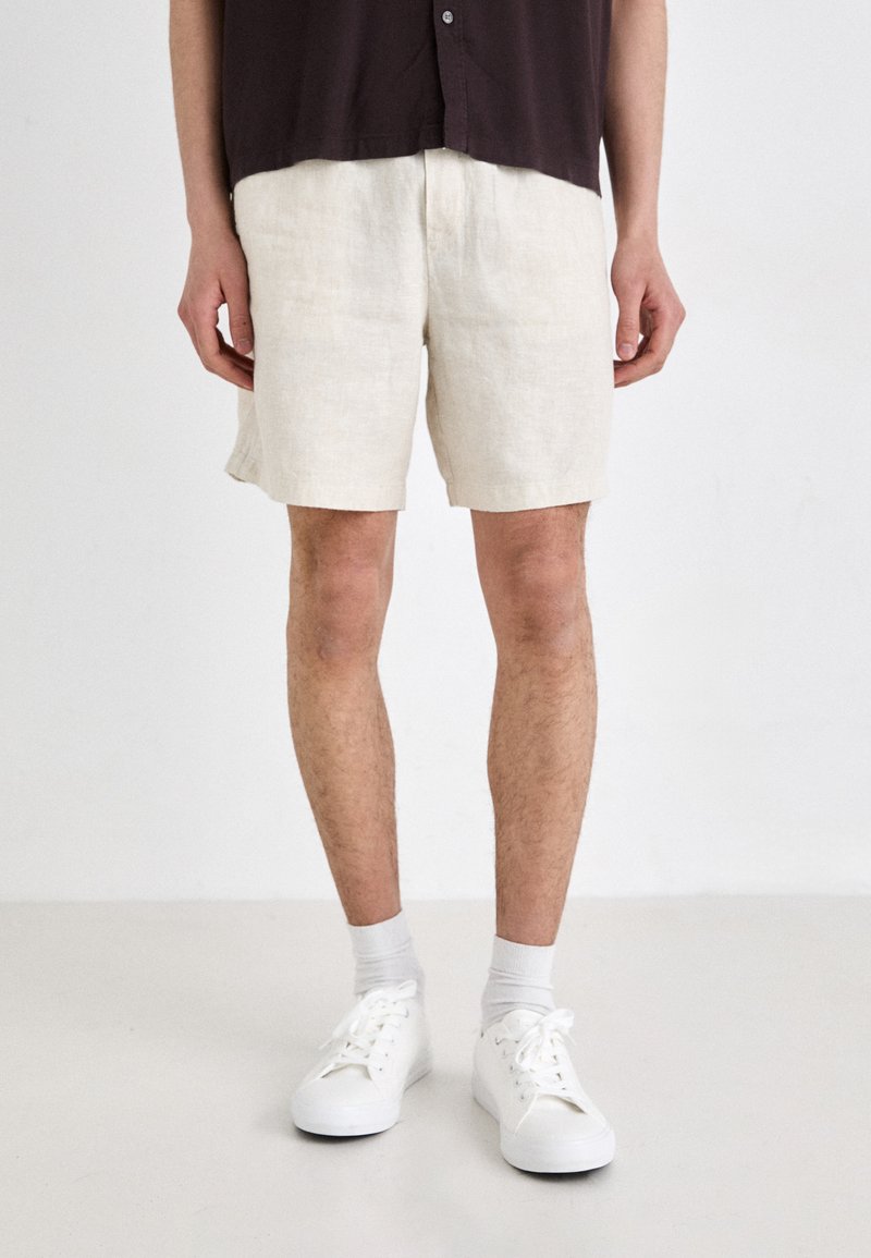 Szorty lniane w kolorze off-white, z luźnym krojem i długością do kolan, połączone z białymi sneakersami i skarpetkami do kostek.