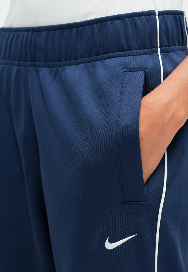 Pantaloni sportivi navy con vita elastica, tasche laterali e strisce bianche a contrasto. Logo Nike bianco in basso.