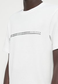 Λευκό βαμβακερό μπλουζάκι με μαύρο και γκρι ριγέ σχέδιο στο στήθος και το κείμενο "JACK&JONES". Κοντά μανίκια και λαιμός τύπου crew.