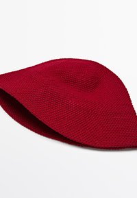 Red knit bucket hat with textured weave, wide flexible brim, displayed on a white background.