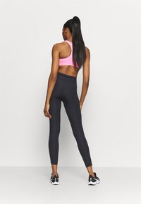 Leggings negros de cintura alta combinados con un sujetador deportivo rosa, mostrando un diseño ajustado y una textura suave, visto desde atrás.