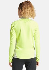 Haut de sport à manches longues en jaune fluo, tissu léger, design ajusté avec des panneaux latéraux gris, texture lisse et col montant.