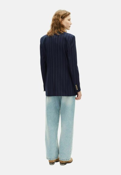Blazer a righe navy con maniche lunghe, dettagli con bottoni dorati, abbinato a jeans a gamba larga blu chiaro e calzature marroni.