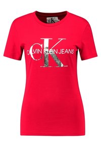 Červené tričko s krátkým rukávem vyrobené z bavlny, které na přední straně obsahuje velké stříbrné logo "CK" a text "CALVIN KLEIN JEANS" v bílé barvě.
