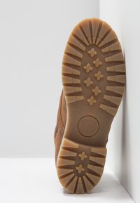 Chaussure en daim marron avec une semelle extérieure en caoutchouc. La bande de roulement présente un motif à losanges pour une meilleure adhérence. Pointure 37 indiquée sur la semelle.