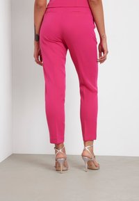 Fitte roze broek met een gladde textuur en taps toelopende pijpen, met twee achterzakken en gecombineerd met zilveren hoge hakken.