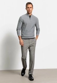 Maglione grigio con zip sul collo e texture a coste, abbinato a pantaloni grigio chiaro e scarpe nere. Design semplice, silhouette aderente.