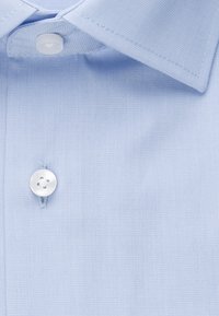 Lichtblauw overhemd met witte knopen en een netjes gestikte kraag, met zichtbare stofstructuur en knoopdetails.