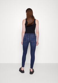 Vaqueros ajustados de denim azul oscuro con una textura suave, que cuentan con dos bolsillos traseros y una cintura de altura media, combinados con zapatos de plataforma negros.