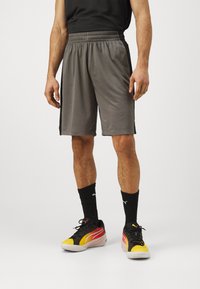 Pantalones cortos deportivos grises con una tela texturizada, cintura elástica y una franja negra en los laterales, combinados con zapatillas deportivas negras y amarillas.