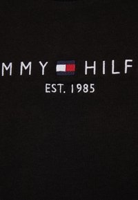 Schwarzes Baumwoll-T-Shirt mit weißer Stickerei "TOMMY HILFIGER" und einem Logo-Tag in Rot, Weiß und Blau, sowie "EST. 1985" darunter.