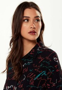 Black shirt featuring colorful, handwritten-style embroidery in red, white, and turquoise, with a textured fabric and a collared design.