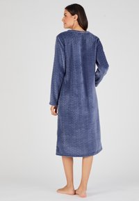 Accappatoio lungo in velluto blu navy realizzato in tessuto morbido, caratterizzato da un motivo a spina di pesce e maniche lunghe. Presenta un colletto rotondo e una lunghezza fino al ginocchio.