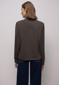 Top de manga larga color marrón oscuro con cuello alto, textura suave y un corte holgado. Combinado con pantalones anchos de mezclilla azul.