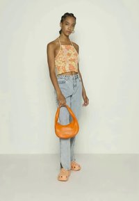 Modelo a usar um top halter cropped floral, jeans azuis claros e uma mala de couro laranja. O calçado são tamancos de cor clara. Fundo liso.