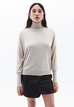 Maglione beige a collo alto con vestibilità ampia, maniche lunghe e orlo a costine, abbinato a una mini gonna nera. Tessuto liscio, design informale.
