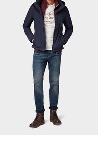 Chaqueta navy con capucha, camiseta gris y jeans azules. Botas marrones con cordones. Diseño casual con interior en contraste y detalles de costura.