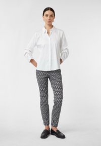Biała koszula z długim rękawem i kołnierzykiem, w zestawieniu z czarno-białymi, wzorzystymi spodniami slim fit oraz czarnymi mokasynami. Prosty design.