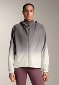 Ľahká bunda s kapucňou s ombre dizajnom, ktorý prechádza z tmavošedej do svetlošedej. Obsahuje elastické manžety a predný zips.