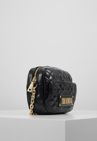 Svart quiltad läderväska med kedjestrapp i guldton, rektangulär form, framficka med logoplåt och dragkedjestängning.