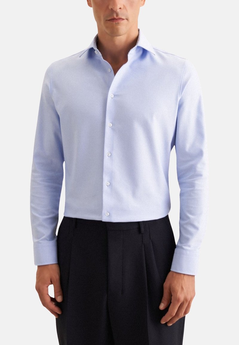 Camisa de manga larga azul claro con botones en la parte delantera y un cuello estructurado. Fabricada con una tela suave que presenta sutiles detalles de textura.