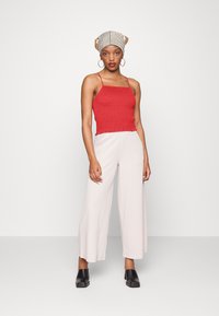 Top cropped vermelho com pregas, calças largas bege, mules pretos com salto quadrado e um lenço riscado. Design simples com texturas suaves.