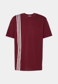Burgundské bavlněné tričko s bílým pruhovaným designem na levé straně, krátkými rukávy a kulatým výstřihem. Přítomný jemný detail loga.
