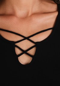 Czarny top z głębokim dekoltem, ozdobiony krzyżującymi się detalami i gładką teksturą. Tkanina wydaje się miękka i dopasowana.