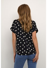 Marinebluse med cremede prikker, korte ærmer, afslappet pasform og rundet kant. Båret med blå jeans, der viser et afslappet look.