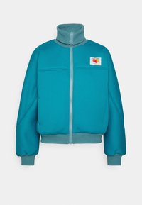 Turkos zipjacka med hög krage, mesh-textur, två framfickor och en logotyp patch på vänster bröst. Ribbat ärm och nederkant.