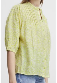 Blusa verde chiaro con un motivo texturizzato, frontale plissettato, maniche corte e chiusura a bottoni. Design casual con scollatura arrotondata.