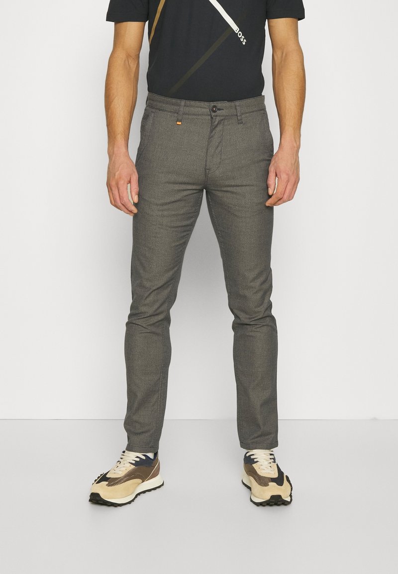 Grå skräddarsydda byxor med en slät textur, slim fit, subtilt mönster och knappstängning; tillsammans med en svart grafisk t-shirt och sneakers.