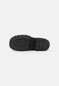 Black rubber sole with a textured tread pattern for traction, featuring a rounded shape and a logo embossed near the heel.