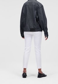 Black and white patterned jacket with a relaxed fit, paired with white slim-fit pants and black shoes with a label on the heel.