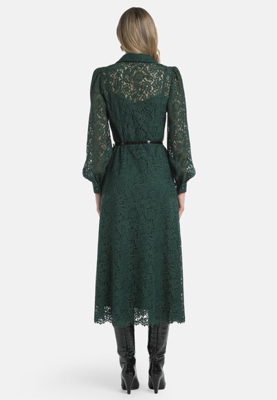 Rochie lungă din dantelă verde, cu talie ajustată și mâneci bufante, având un spate transparent și un tiv cu margini ondulate, asortată cu cizme negre până la genunchi.