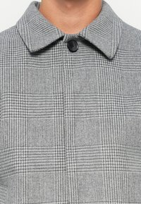 Grijze geblokte jas met een klassieke kraag, textiel met uiteenlopende patronen en een zwarte knoopsluiting.