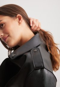 Zwarte leren jas met een brede kraag, drukknoopsluiten en gedetailleerde stiksels. Glad textuur met een getailleerde silhoutte en een op maat gemaakt ontwerp.