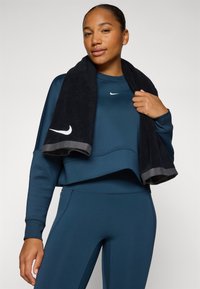 Sweatshirt de sport bleu marine avec un design court et le logo Nike, associé à un legging assorti. Une serviette noire avec un contour gris est drapée sur l'épaule.